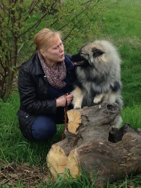 Renate hockt im Garten an einem Baumstamm und schmust mit einem Wolfsspitz